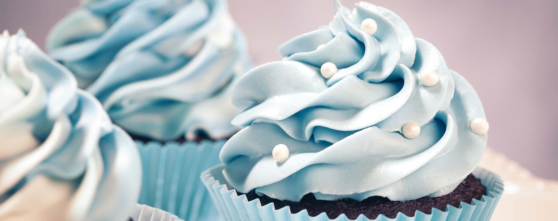 A close up of chocolate cupcakes with light blue icing, there are edible pearls decorating the cupcakes