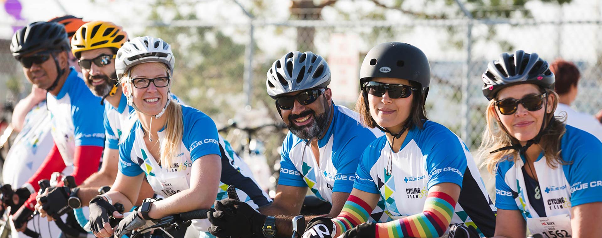 Group of six Alberta Blue Cross employees in matching race tops are leaning against the front handle bars of their bicycles in preparation for a race.