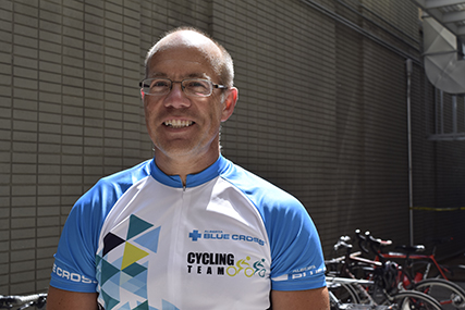 Barry in a Team Alberta Blue Cross cycling shirt, standing in front of a bicycle rack.