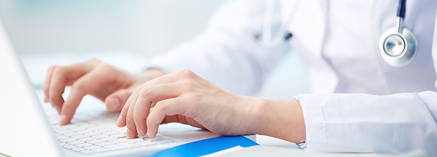 A close up of a doctor using a laptop. There is a stethoscope hanging around their neck. You cannot see their face.