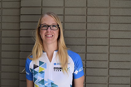 Janelle standing in front of a brick wall in a Team Alberta Blue Cross cycling shirt