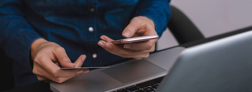 A close up of someone holding a rose gold iPhone and a credit card while sitting in front of a sleek laptop.