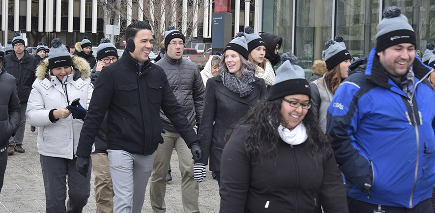 A large, multiracial group of Alberta Blue Cross employees in winter coats, mitts and toques are walking in downtown Edmonton, AB.
