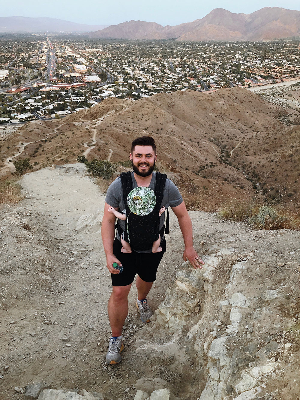 The husband of Lindsey Smith wearing a baby carrier with their infant while he hikes.