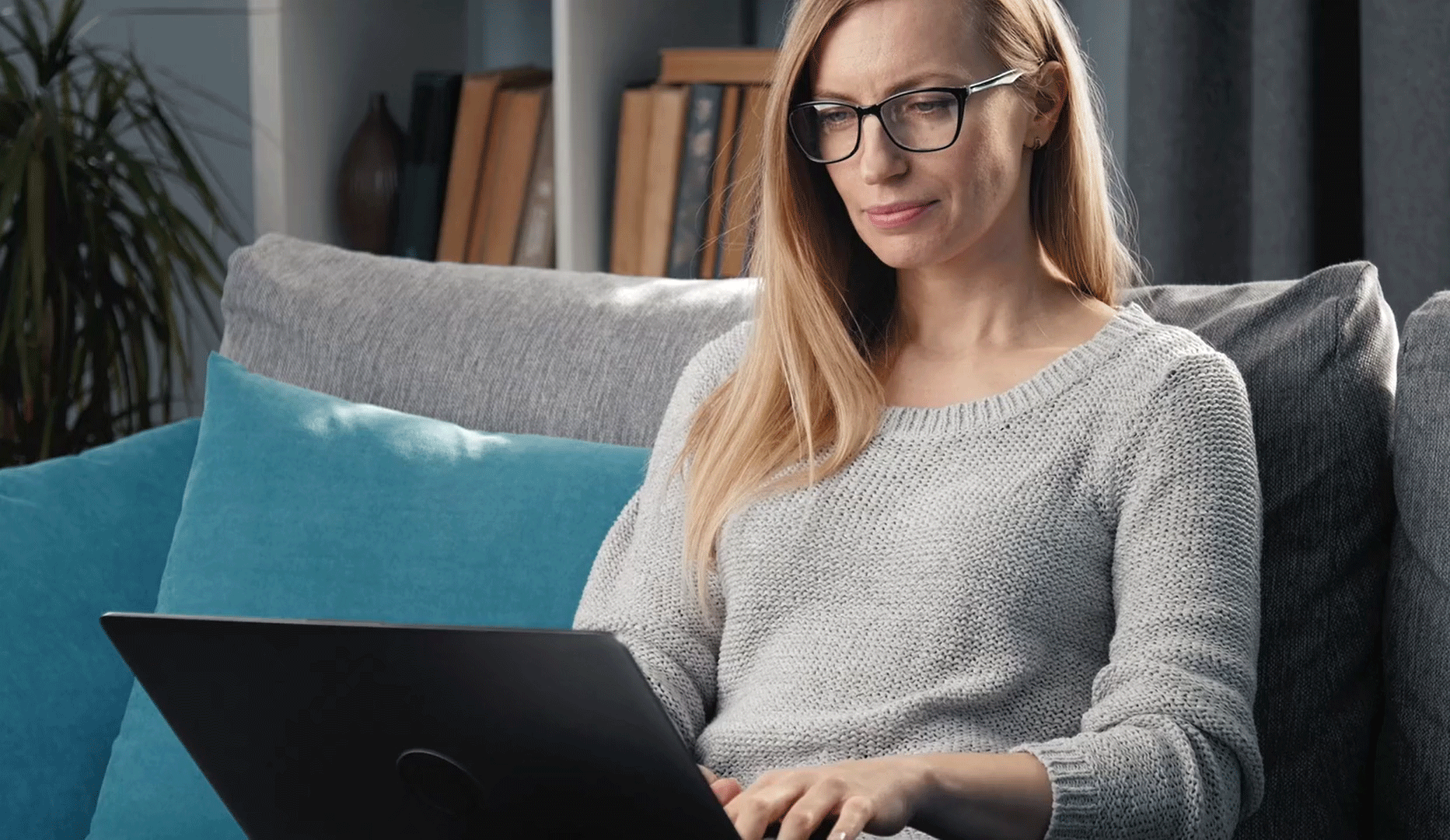 A woman sits on a couch with her laptop in her lap.