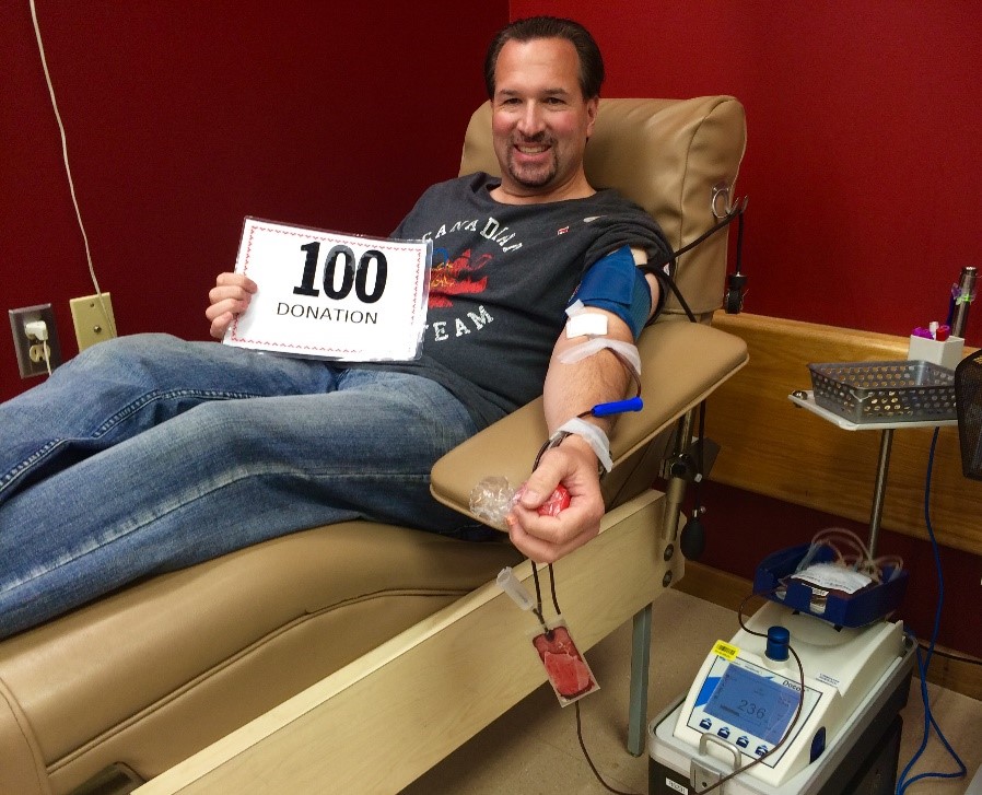 Brian Geislinger donating blood holding "100 donations" card