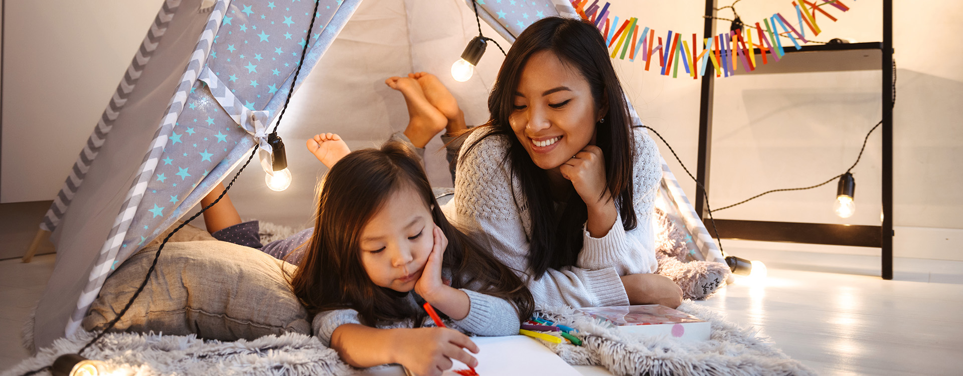 Image of a beautiful young asian woman with her little daughter having fun drawing in album on floor.