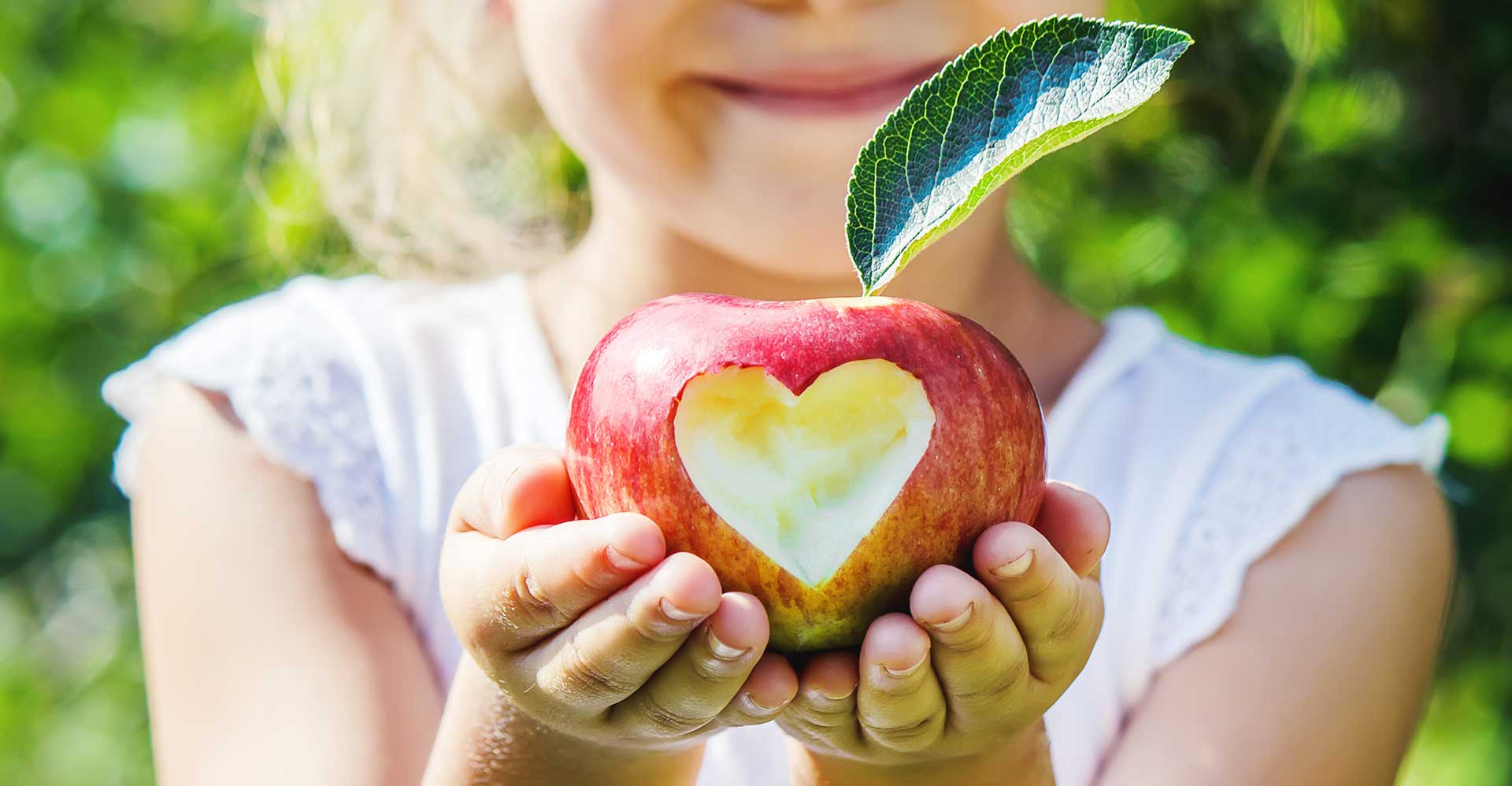 Child holding an apple with heart shape carved into the front.
