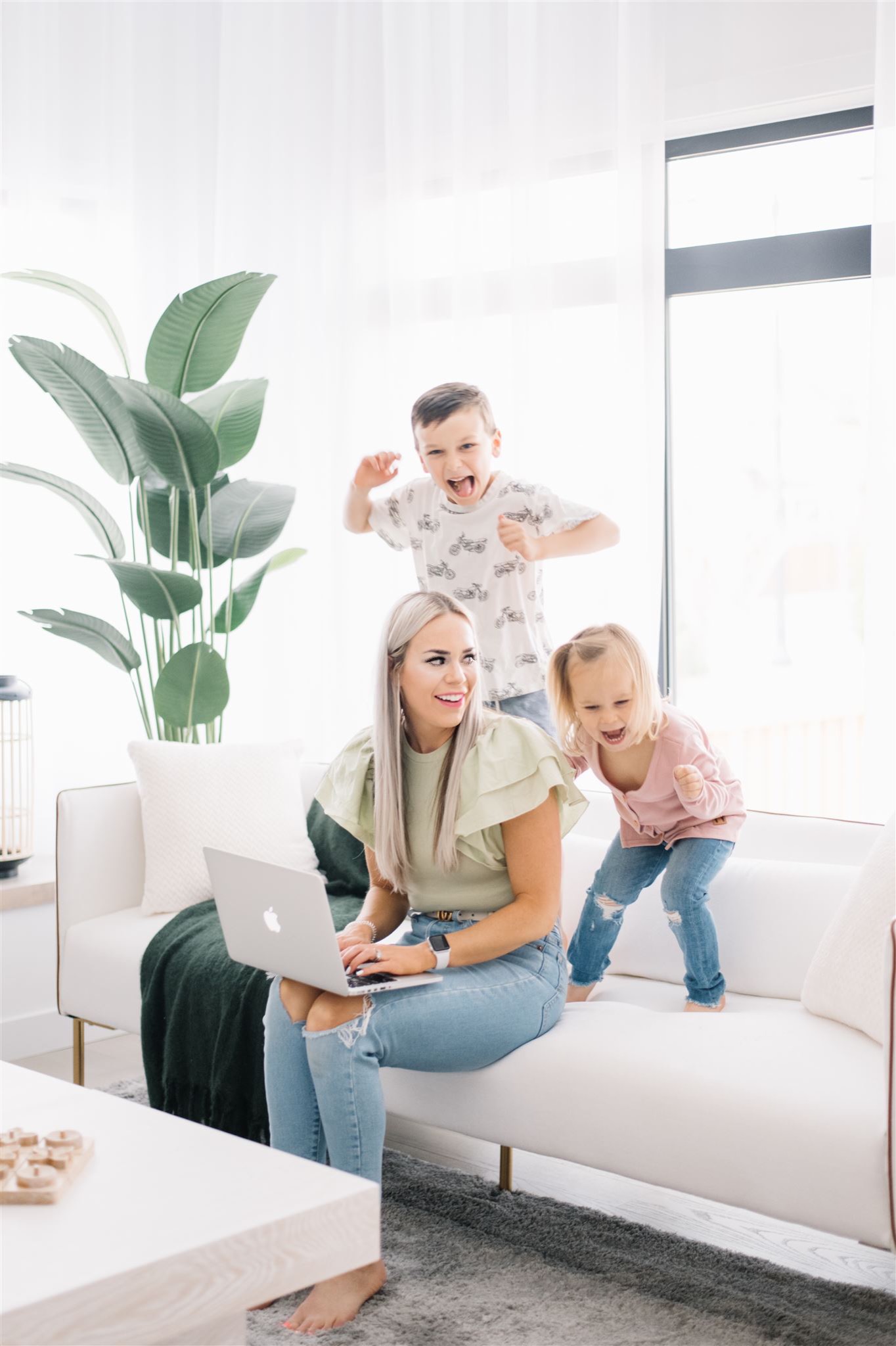 Richelle on her computer with her two children playing on the couch behind her.