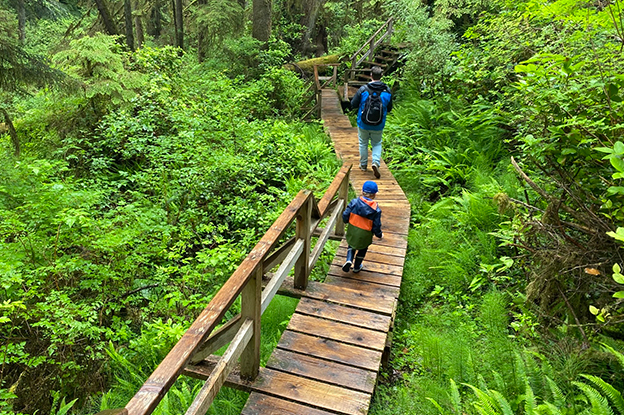 A kid following his father during a hike on a trail in a jungle in Tofino, British Columbia.