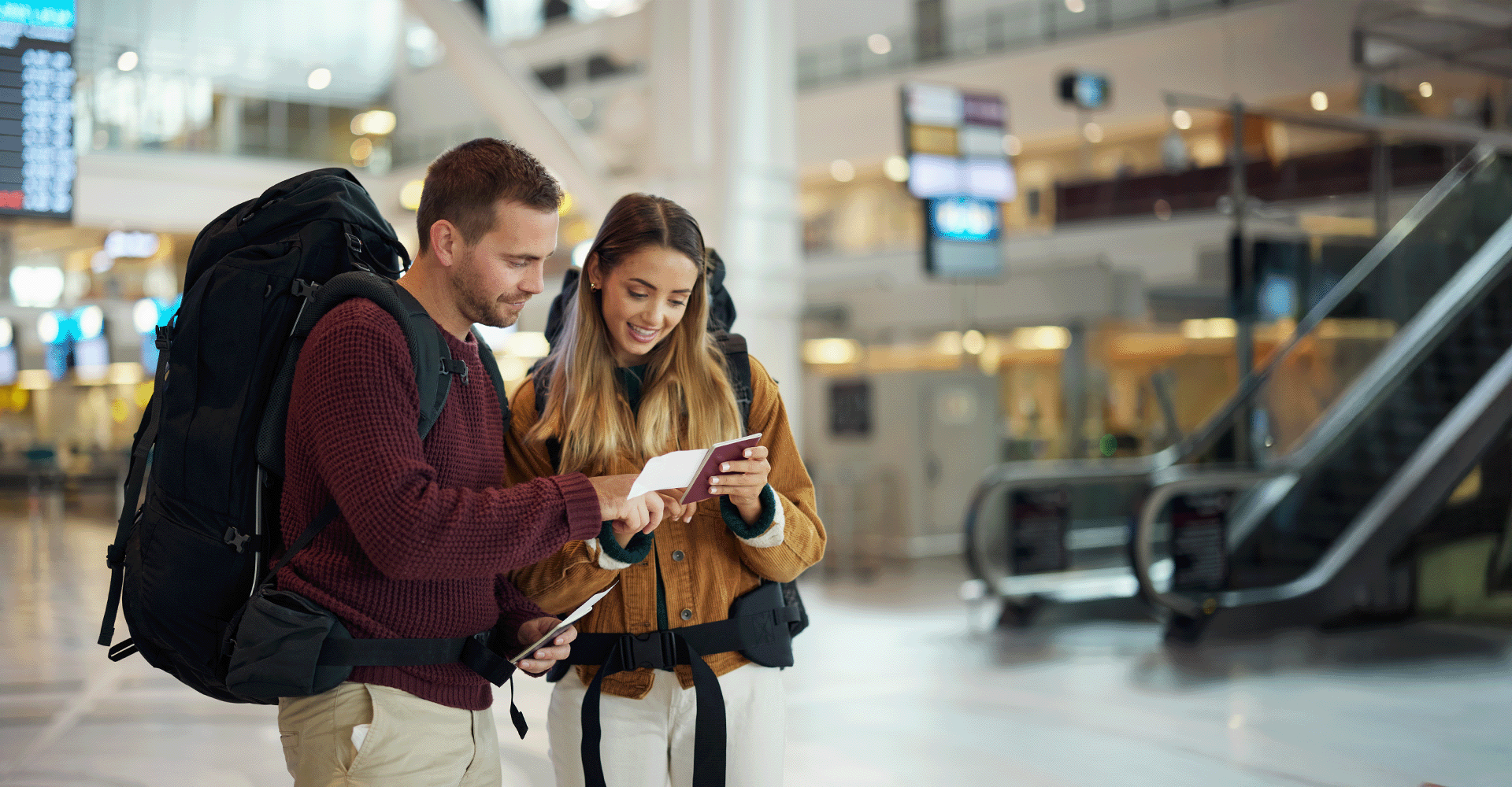 A young couple with backpacks looking at their passports and tickets in an airport terminal.