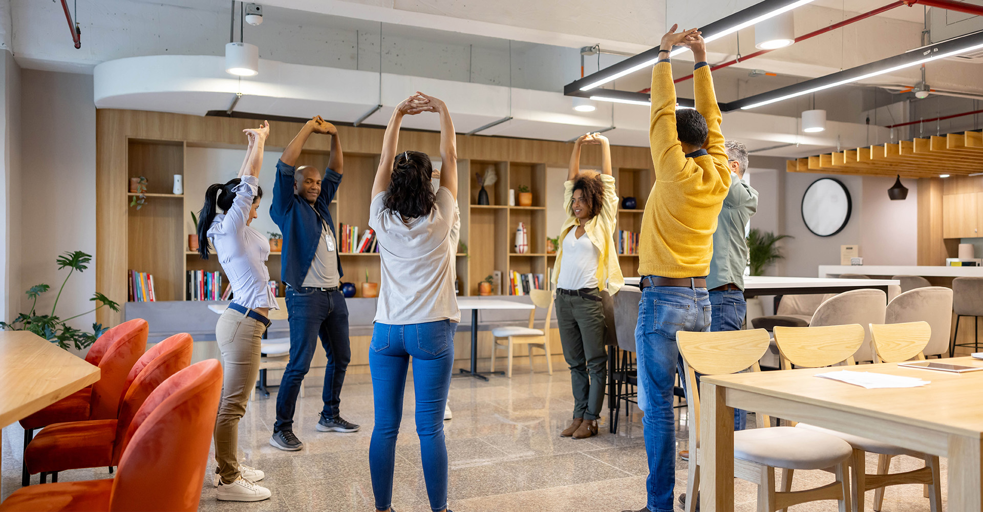 Employees participating in a group exercise class at work, engaging in stretches in a bright, open office space.