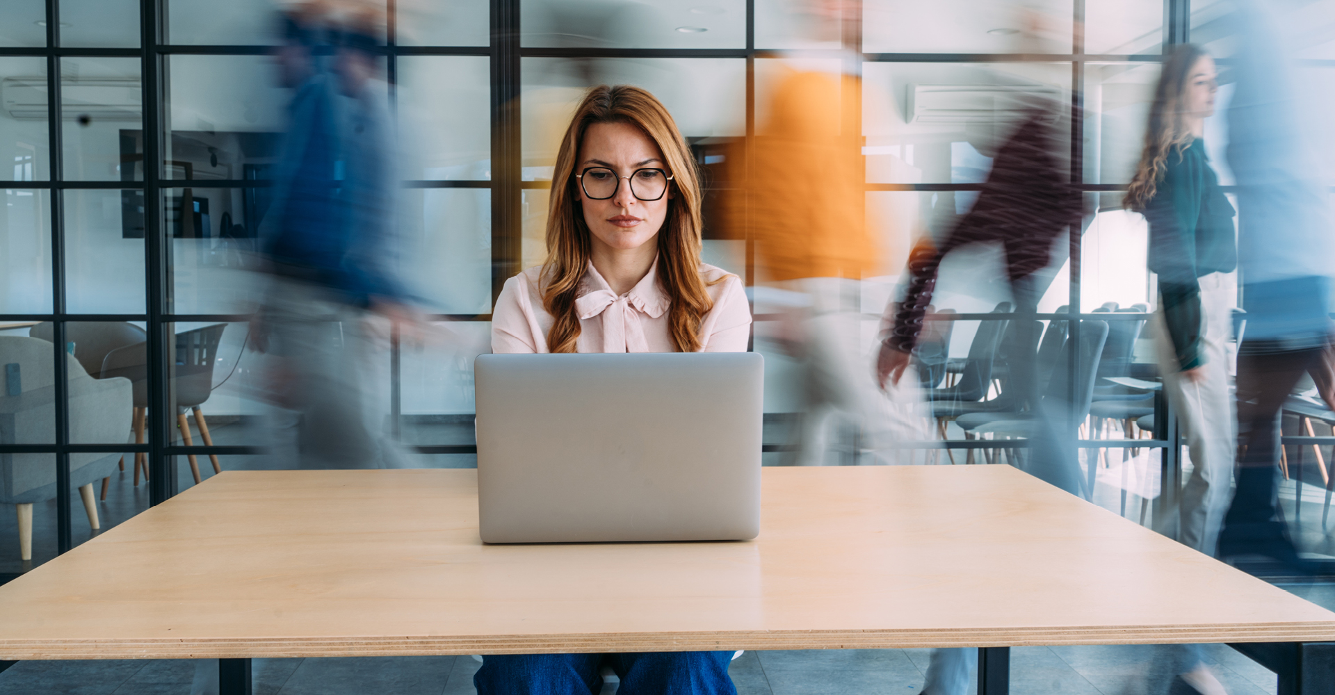 Woman focused on her laptop in an office, while coworkers walk past creating a motion blur.